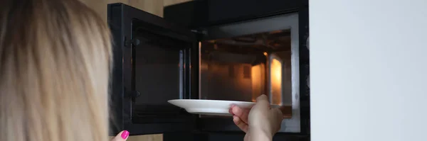 Mulher colocando prato de comida no microondas em casa close-up — Fotografia de Stock