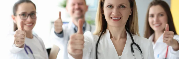 Mujer médico mostrando pulgar hacia arriba contra el fondo de colegas — Foto de Stock