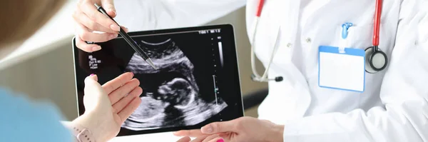 Doctor showing patient woman ultrasound scan of fetus on digital tablet closeup