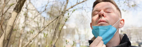 Hombre caminando en el parque y quitándose la máscara protectora de su cara — Foto de Stock