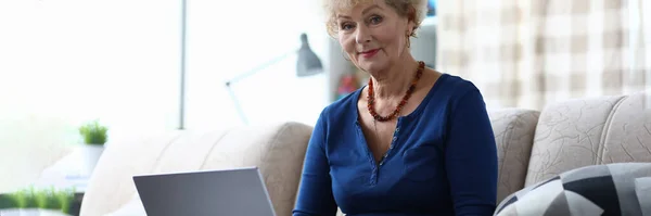 Elderly woman with laptop is sitting on couch — Stock Photo, Image