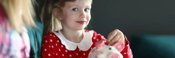 Bambina con sua madre getta moneta nel salvadanaio rosa — Foto Stock