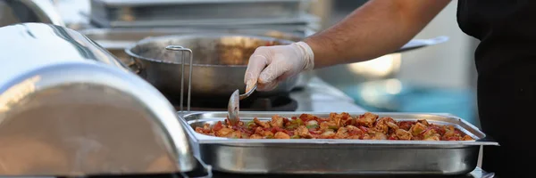 Mężczyzna kucharz w rękawiczki miesza mięso gulasz z warzywami z łyżka — Zdjęcie stockowe