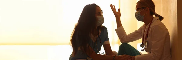 Two tired doctors in medical masks in corridor of hospital