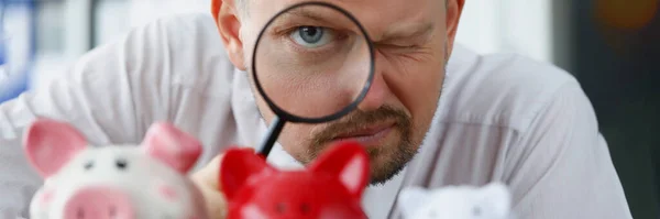 L'homme regarde à travers la loupe à la tirelire — Photo