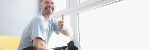 Retrato de homem sorridente segurando halteres e mostrando polegares para cima gesto — Fotografia de Stock