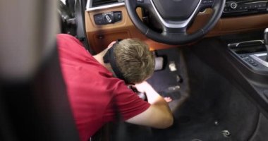 Erkek tamirci 4K filminin altında arabanın içini süpürüyor.