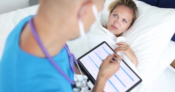 Γιατρός κάθεται δίπλα άρρωστος ασθενής ξαπλωμένος στο κρεβάτι και γράφει παράπονα σε ψηφιακή ταμπλέτα 4k ταινία — Αρχείο Βίντεο