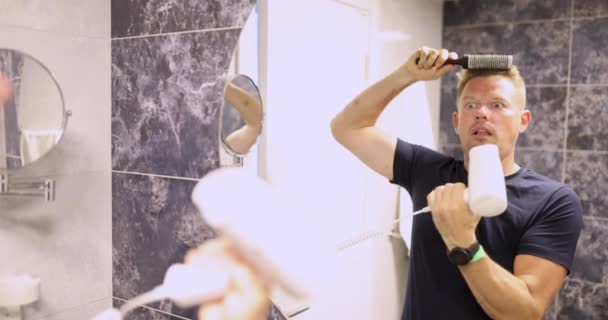 Giovane uomo pettinando davanti allo specchio e soffiando le guance con asciugacapelli film 4k — Video Stock