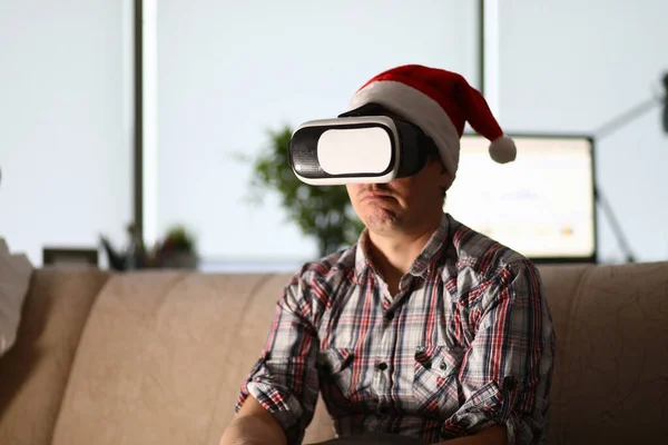 Man met een virtuele bril zit op de bank met de kerstman hoed op — Stockfoto