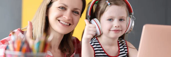Uśmiechnięta kobieta z małą dziewczynką w słuchawkach zajmuje się edukacją online na laptopie — Zdjęcie stockowe