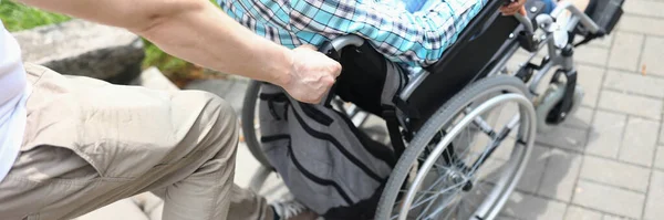 Mężczyzna podnosi kobietę na wózku inwalidzkim na górze — Zdjęcie stockowe