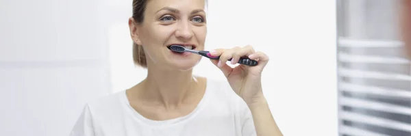 Улыбающаяся женщина чистит зубы перед зеркалом — стоковое фото