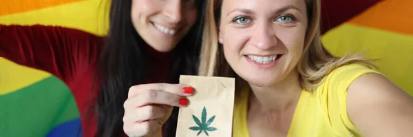 Dos mujeres sonrientes sosteniendo bandera lgbt y paquete de marihuana —  Fotos de Stock