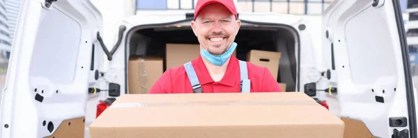 Man courier holds cardboard box on background of car — Stock Photo, Image