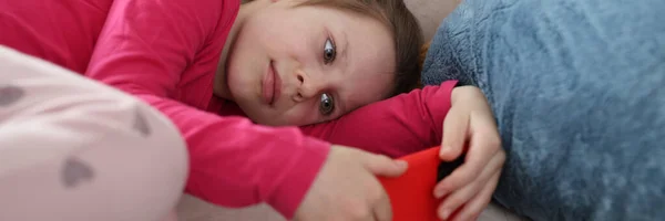 Little girl lies on couch and looks at smartphone screen — Stock Photo, Image