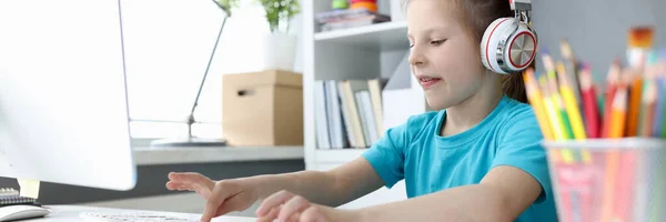 Niña en los auriculares delante de la computadora está escribiendo en el teclado —  Fotos de Stock