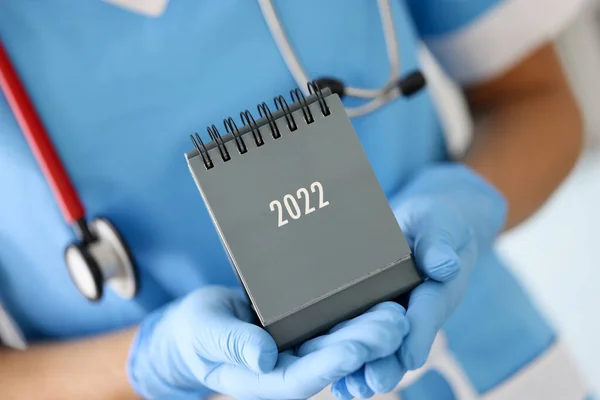 Doctor in medical rubber gloves holding desk calendar for 2022 closeup