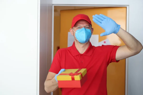 Αρσενικό κούριερ σε προστατευτική ιατρική μάσκα και γάντια από καουτσούκ κρατώντας δώρο — Φωτογραφία Αρχείου