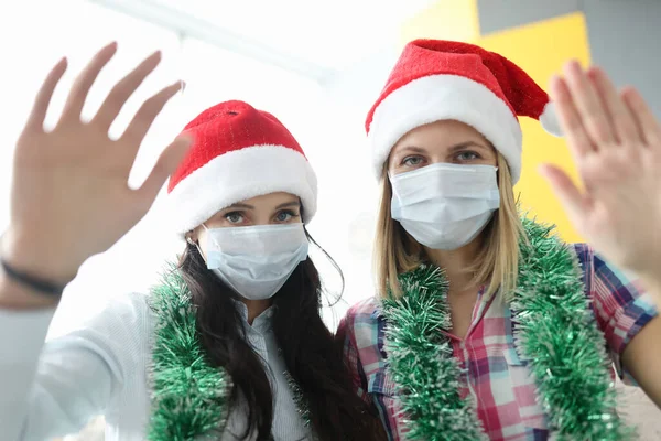 Vrouwen in beschermende medische maskers en kerstman hoeden zwaaien naar de camera — Stockfoto