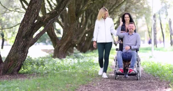 Souriant jeune femme et homme heureux en fauteuil roulant sur la promenade dans le parc 4k film — Video