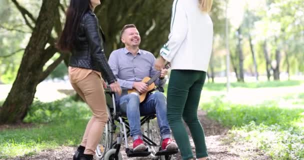 Ευτυχισμένος άντρας σε αναπηρική καρέκλα παίζει κιθάρα δίπλα στο χορό χαμογελαστή γυναίκα 4k ταινία — Αρχείο Βίντεο