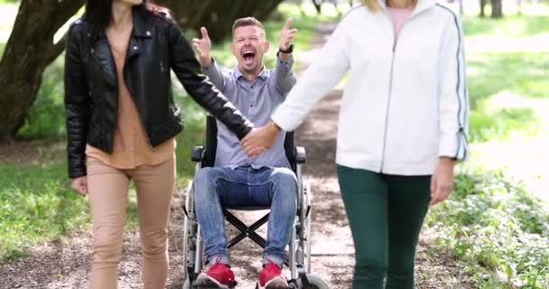 二人の若い女性は離れてから歩く欲求不満男座っています車椅子4k映画 — ストック動画