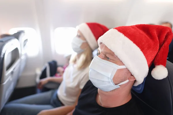 Mężczyzna i kobieta w czerwonych kapeluszach Świętego Mikołaja i ochronnych maskach medycznych latających w samolocie — Zdjęcie stockowe