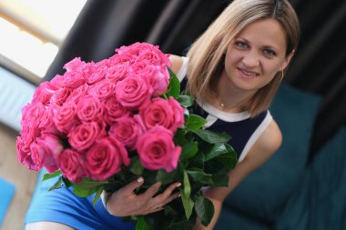 Kanepede oturan ve elinde büyük bir buket gül tutan genç bir kadın.