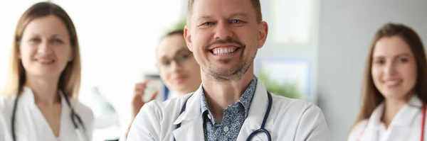 Exitoso hombre sonriente médico de pie en contra de los antecedentes de los colegas en la clínica —  Fotos de Stock