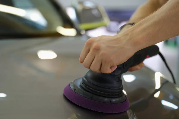 Male hands polishing hood of car with special machine closeup