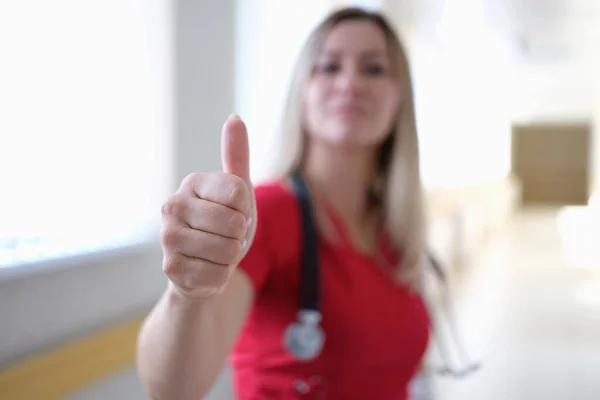 Mulher médico em uniforme vermelho mostrando polegar de perto — Fotografia de Stock