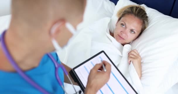 Médico sentado junto a la cama de una paciente joven y escribir información en la tableta digital 4k película — Vídeos de Stock