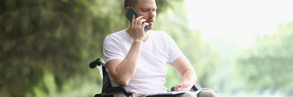 Niepełnosprawny mężczyzna na wózku inwalidzkim rozmawiający przez telefon komórkowy w parku — Zdjęcie stockowe