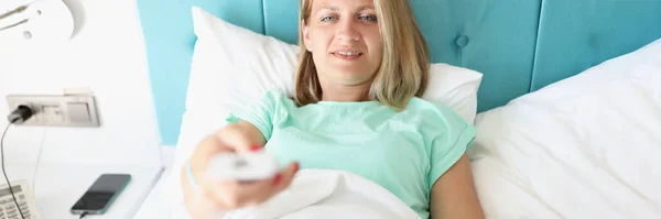Молода жінка лежить в ліжку з телевізійним пультом дистанційного керування в руках — стокове фото