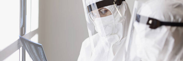 Врачи в защитных противочумных костюмах на экранах смотрят на рентген легких