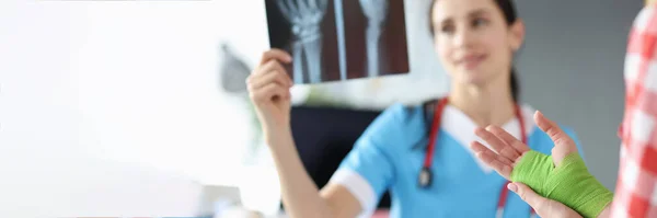 Lekarz bada rentgen dłoni obok pacjenta stoi z zabandażowaną ręką. — Zdjęcie stockowe