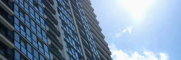 Edificio de varios pisos con muchas ventanas de vidrio de pie sobre el fondo del cielo azul y el sol —  Fotos de Stock
