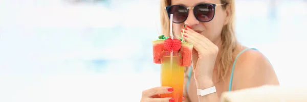 Mujer joven en gafas de sol bebiendo cóctel alcohólico multicolor en la playa — Foto de Stock