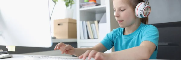 Κοριτσάκι με ακουστικά πληκτρολογώντας στο πληκτρολόγιο του υπολογιστή στο σπίτι — Φωτογραφία Αρχείου