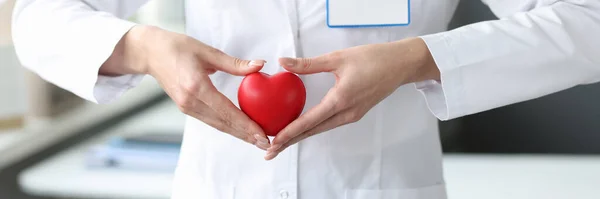 Doctor sosteniendo el corazón de juguete rojo en sus manos en primer plano de la clínica —  Fotos de Stock