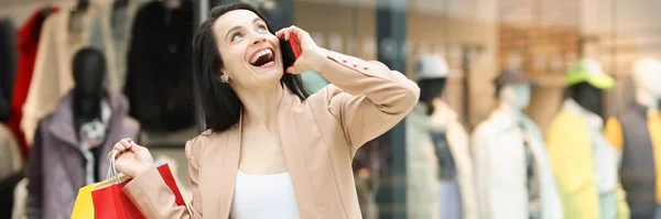 Fiatal boldog nő kezében sok színes papírzacskó és beszél telefonon a boltban — Stock Fotó