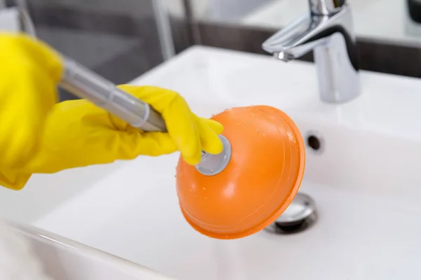 Loodgieter met rubberen handschoenen schoonmaken spoelbak met zuiger in badkamer closeup — Stockfoto