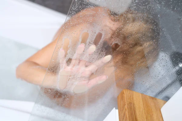 Mujer desnuda sentada en la bañera y sosteniendo su mano en el primer plano de vidrio nebulizado —  Fotos de Stock