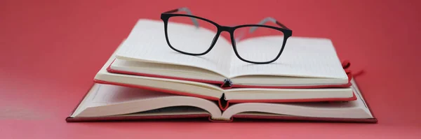 Bril voor gezicht liggend op stapel notebooks op rode achtergrond closeup — Stockfoto