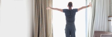 Başarılı adam parlak pencerenin yanındaki yatak odasında duruyor.