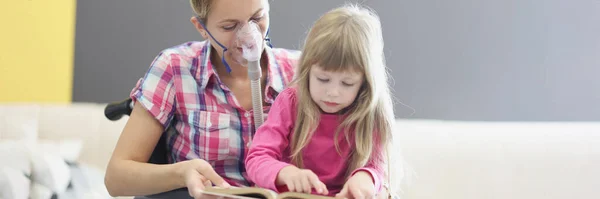 Женщина в инвалидном кресле и кислородной маске читает книгу с маленькой девочкой — стоковое фото