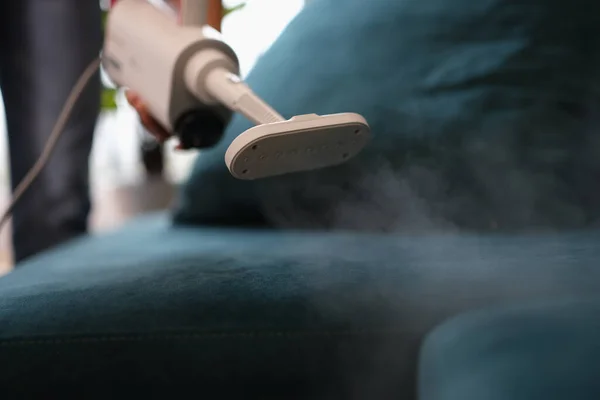 Janitor removes dirt from sofa with steam cleaner