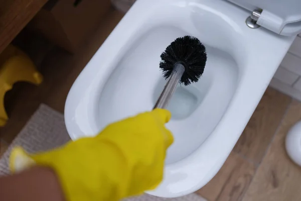 A mão enluvada está limpando o banheiro com a escova de perto — Fotografia de Stock