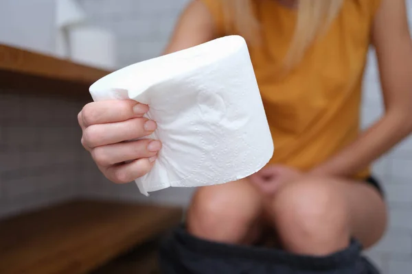Mujer se sienta en el inodoro y sostiene el papel higiénico en las manos — Foto de Stock